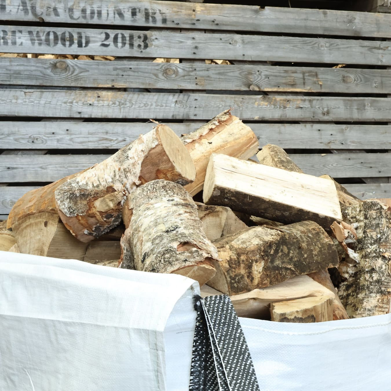 Stack of firewood in a white bag with a wooden potato box in the background