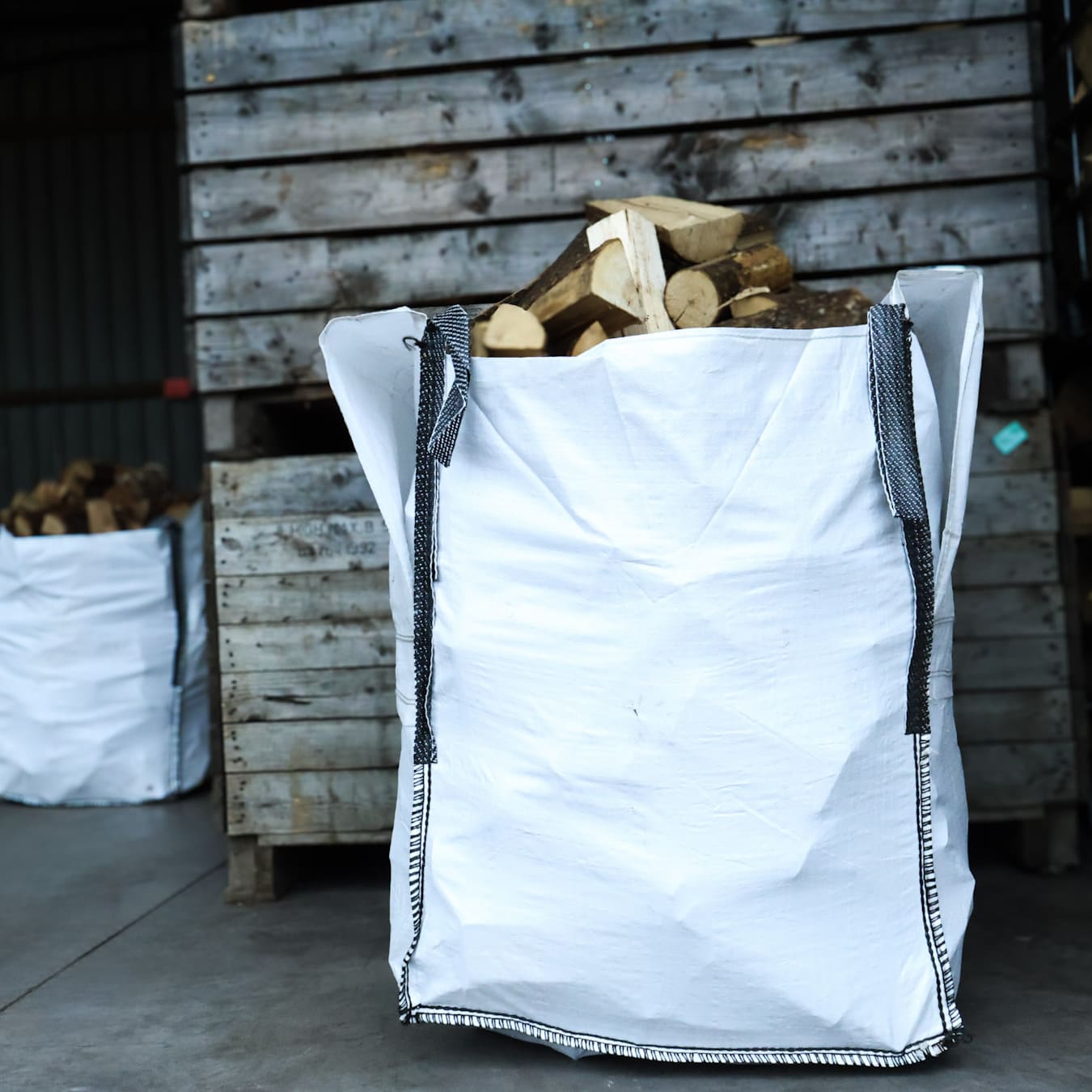 White firewood bag filled with kiln dried ash logs against a wooden wall.