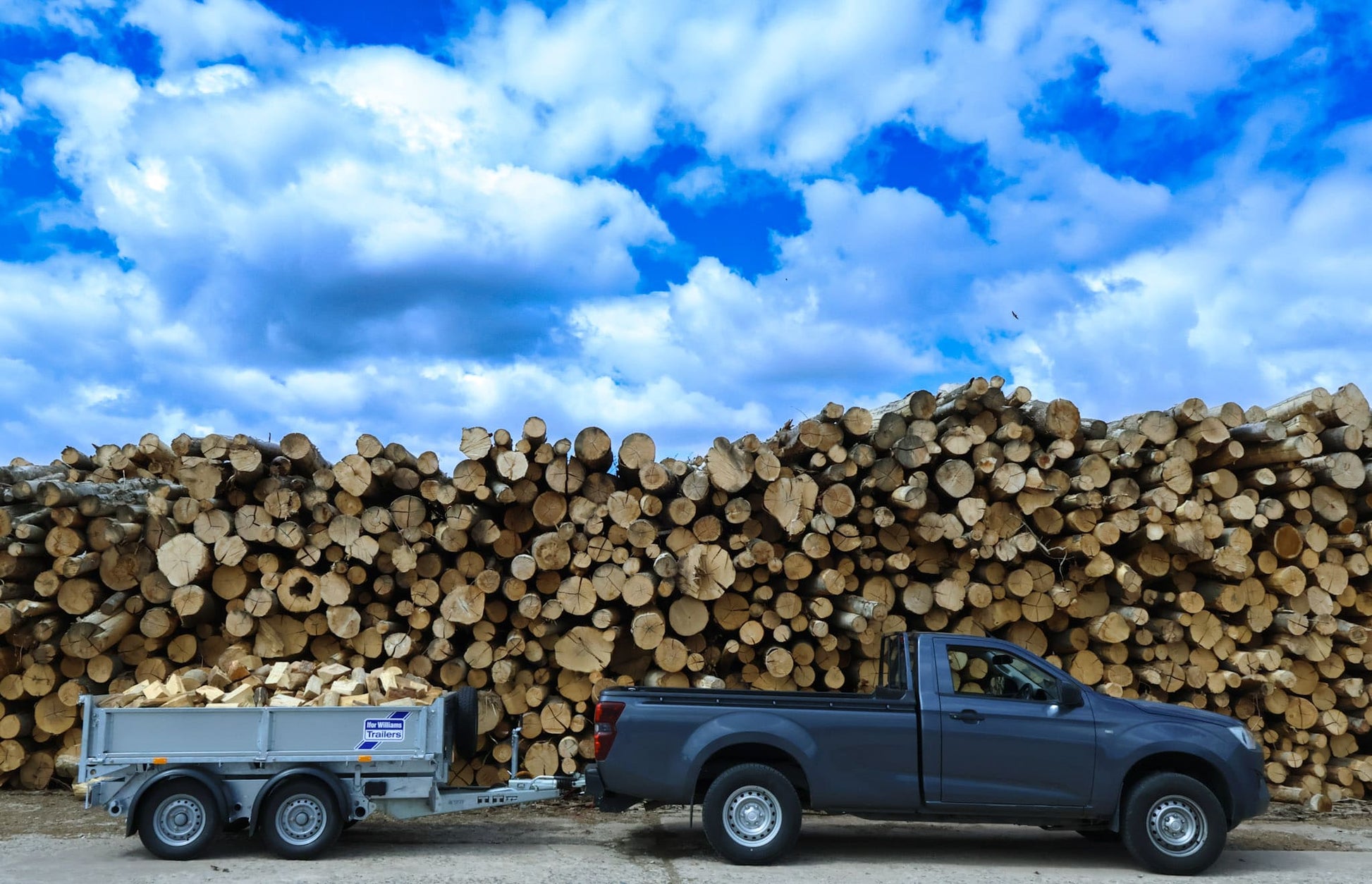 Truck with trailer loaded with logs against a blue sky with clouds