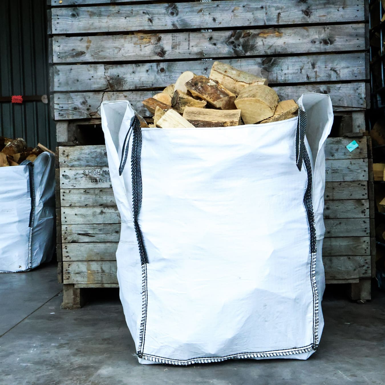 White bulk bag filled with firewood against a wooden pallet background