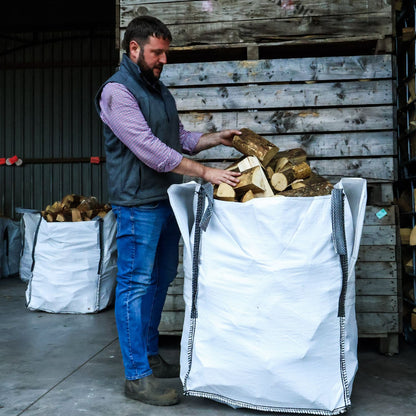 Man loading logs into a large white bag in an industrial setting