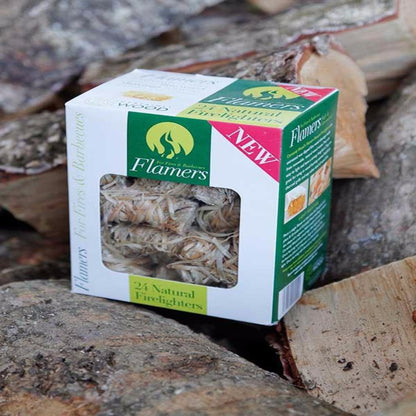 A box of Flamers brand natural firelighters placed on a pile of wood. The box is white with green and red accents and transparent window showing the wood wool firelighters inside.