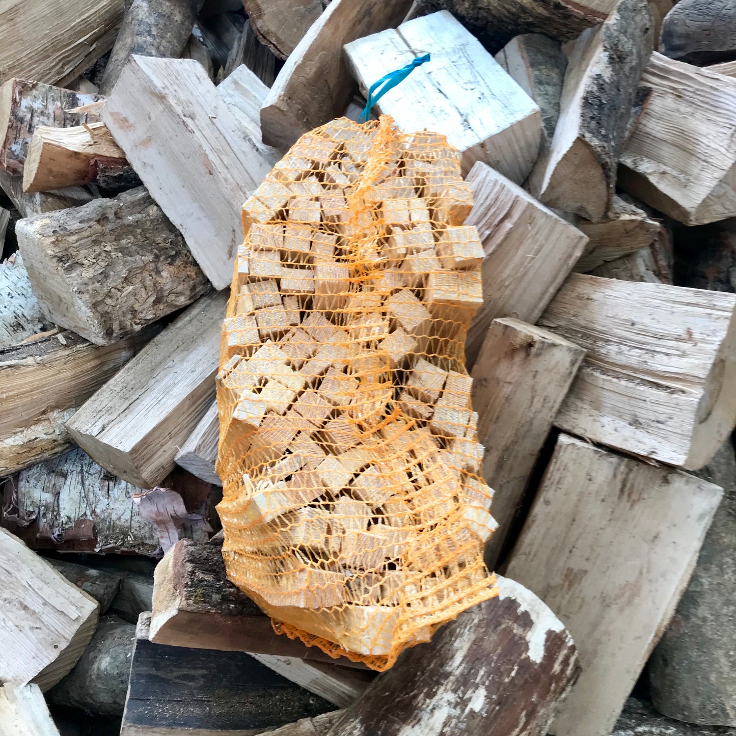 Netted kindling in orange net on log background 
