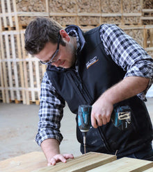 A person working on constructing a wooden log store using a power drill.
