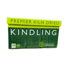 A box of Premier Kiln Dried Kindling Wood placed on a wooden stump with a woodpile in the background.